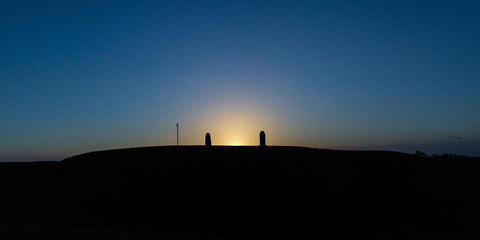 The sun begins too peep above the Hill of Tara between the Lia Fáil and the memorial headstone.