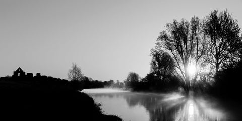 A black and white of a sunrise over the River Boyne at the ruins at Newtown, Trim. The sun casting beautiful shadows of the trees over the river.
